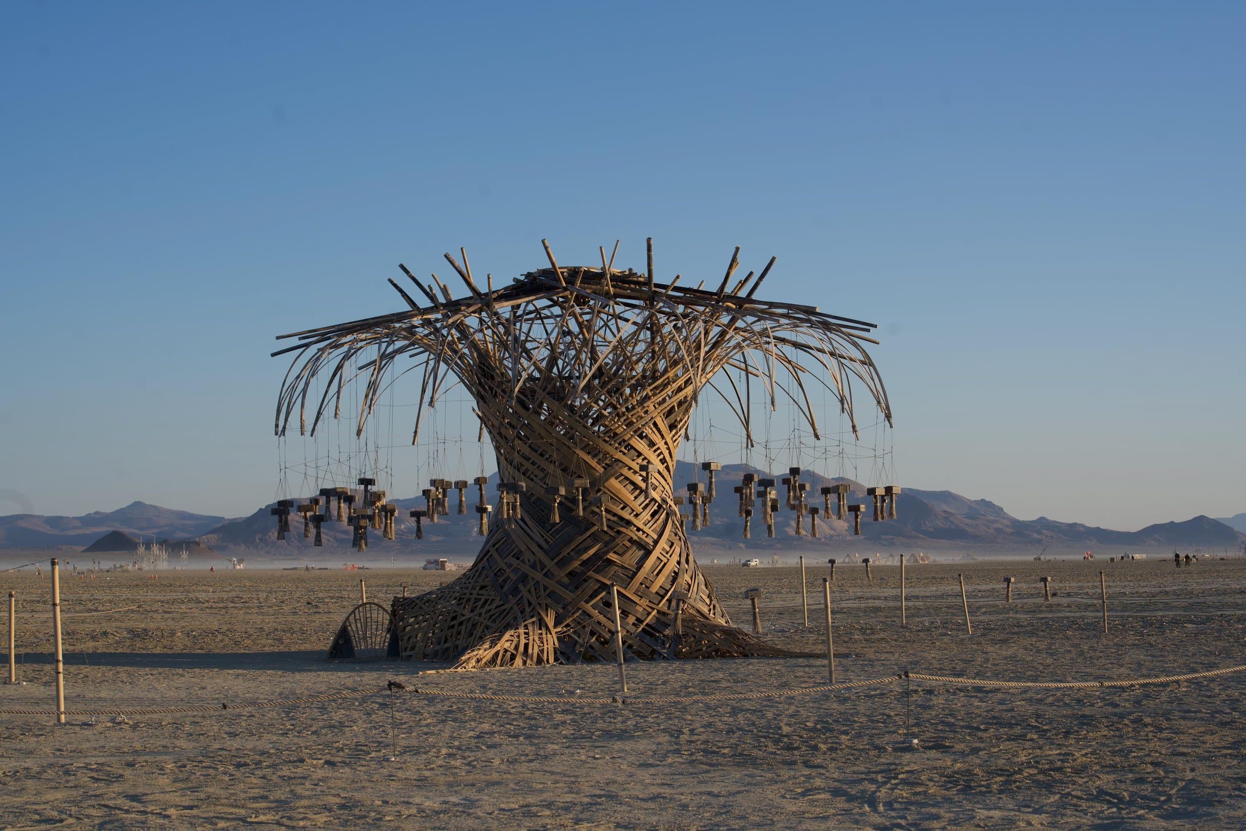 The Resonance Tree alone on the open playa at dawn, chimes hanging still under a clear blue sky