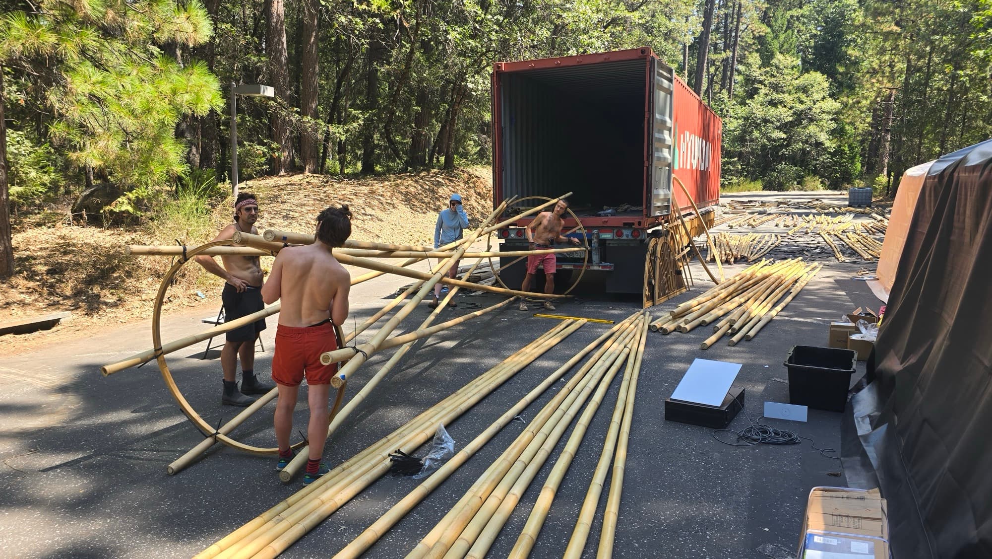 Crew unloading bamboo poles and laminated rings from a shipping container onto a forest road in Nevada City, components laid out across the tarmac