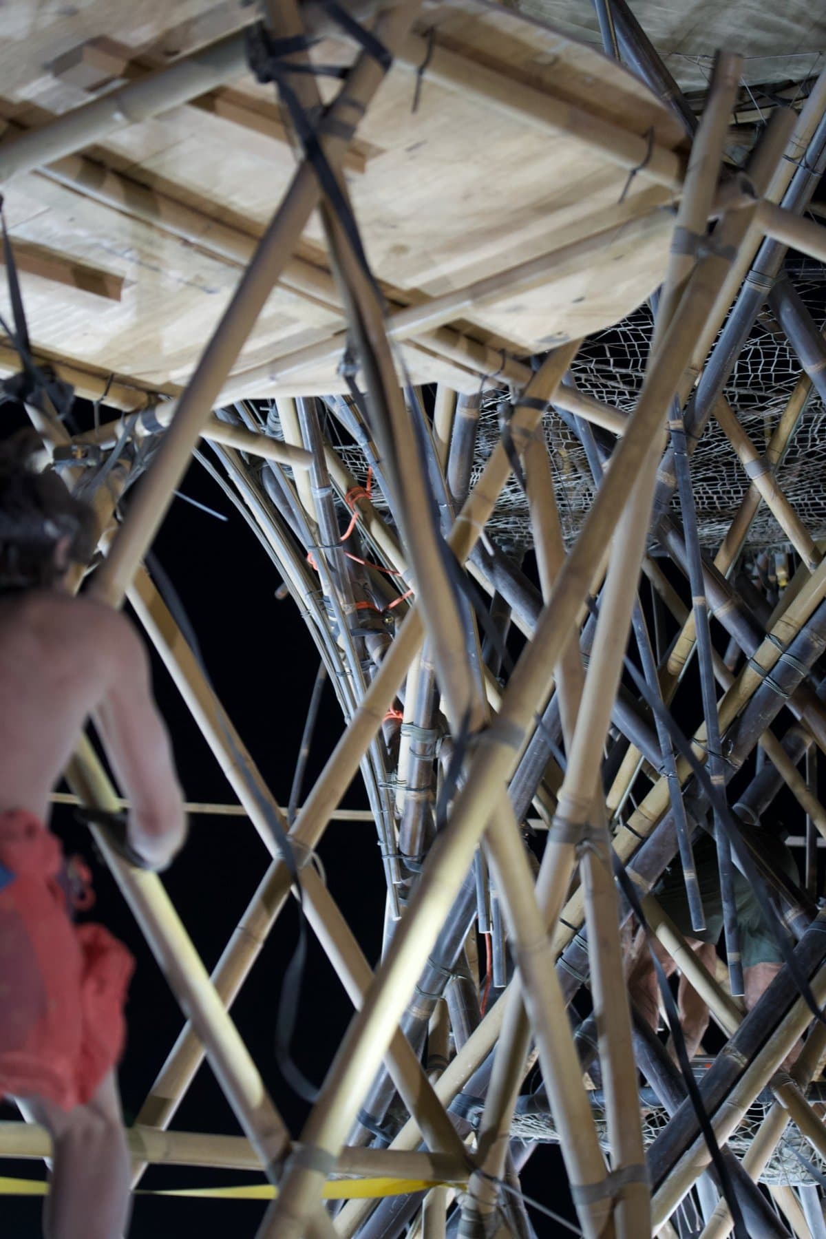Inside the trunk of the Resonance Tree at night, poles crossing overhead under the lashed deck
