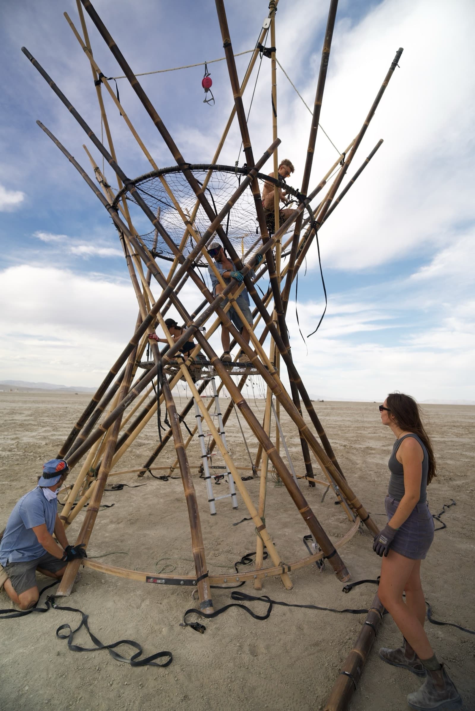Crew members lashing the bamboo trunk lattice on the open playa under a wide sky