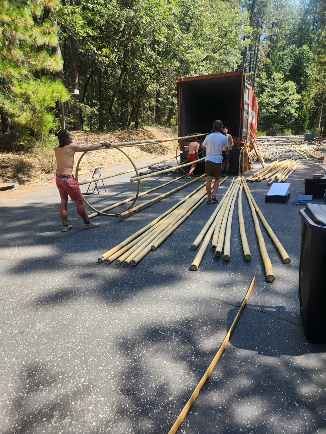 Crew unloading long bamboo poles from the container and laying them out in rows across the shaded road