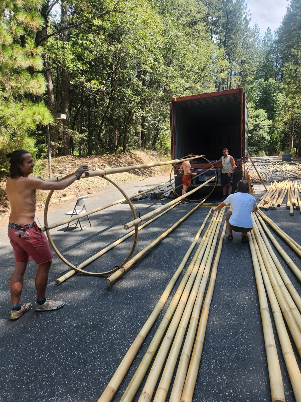 A crew member carrying a laminated bamboo ring and pole away from the open shipping container on a forest road