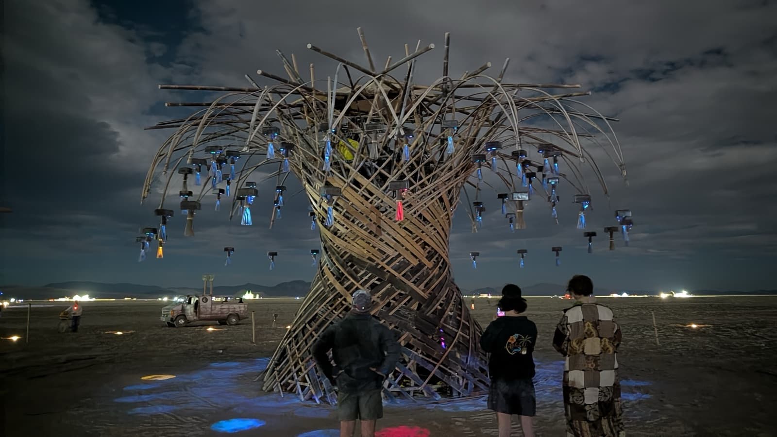 Visitors standing in the glow beneath the lit Resonance Tree at night