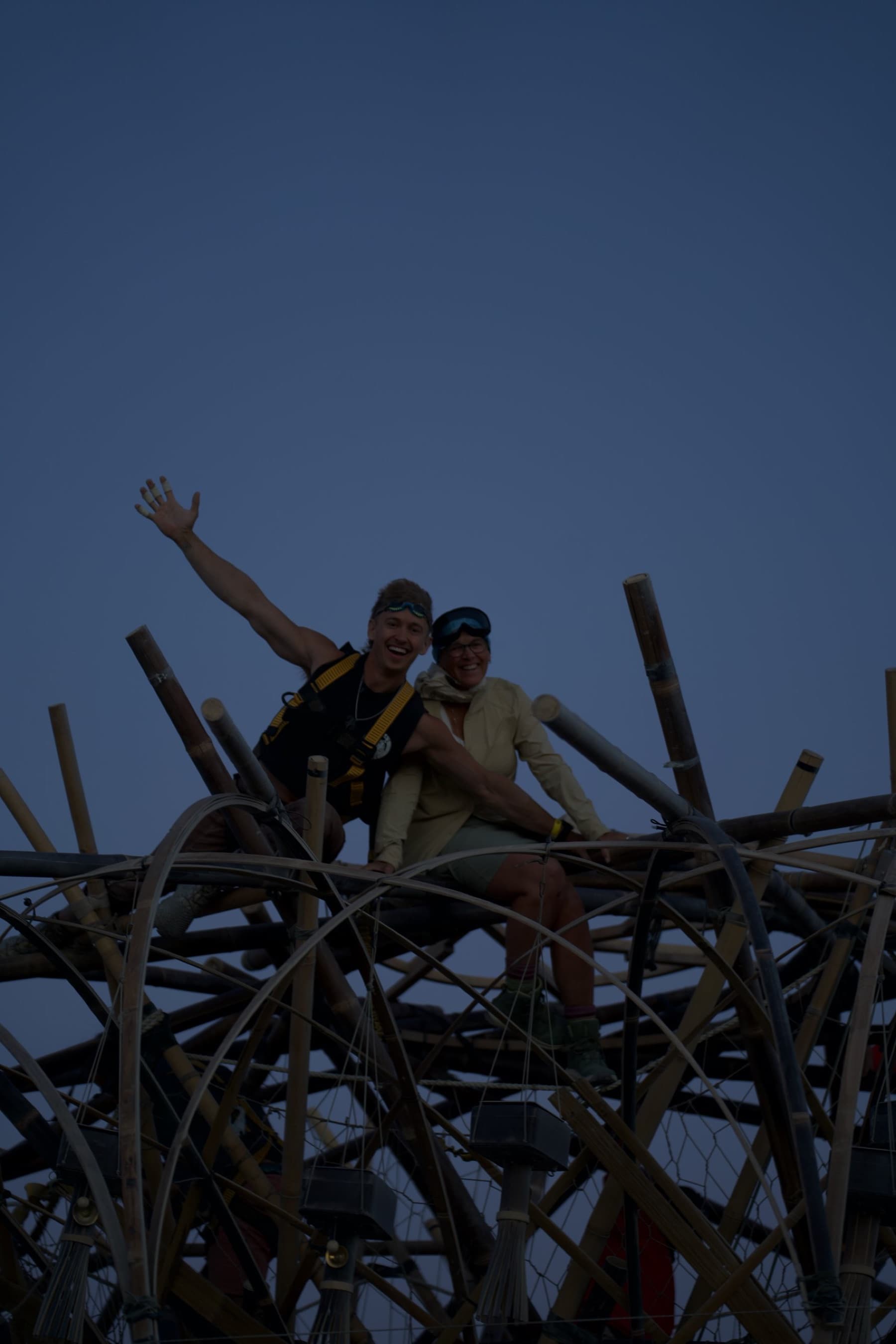 Two crew members on the crown of the finished Tree at dusk, one with an arm thrown up