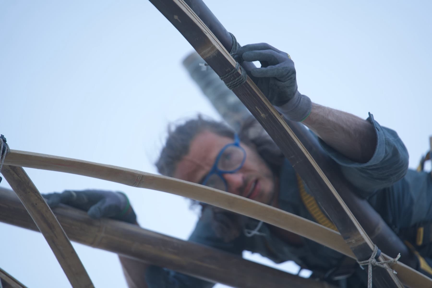 A builder face to face with the bamboo weave, lashing a joint