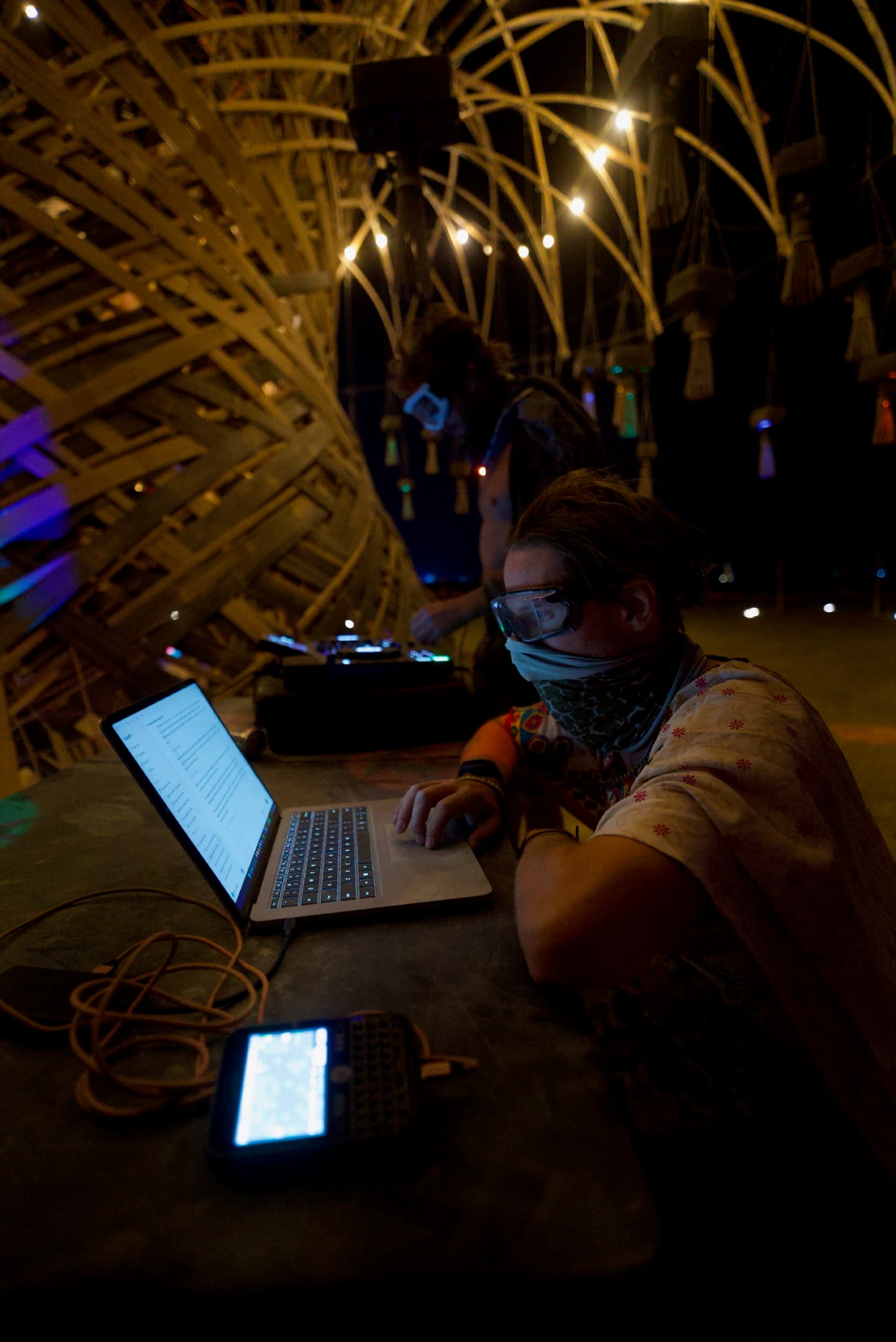 A performer running lights and music from decks beneath the lit Resonance Tree at night