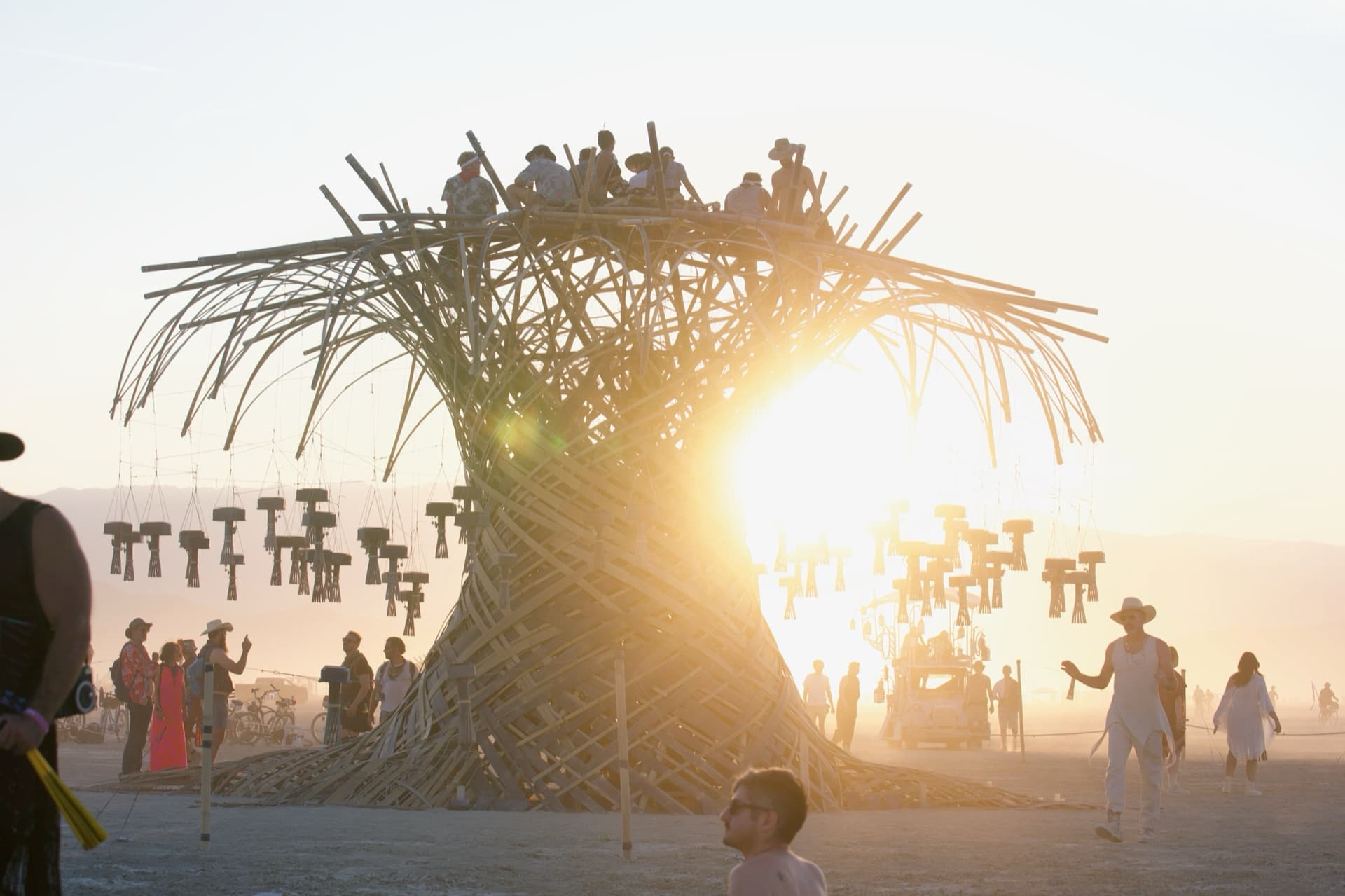 Sunset at Burning Man 2026: a crowd gathered on open playa beneath the Resonance Tree's full lantern crown