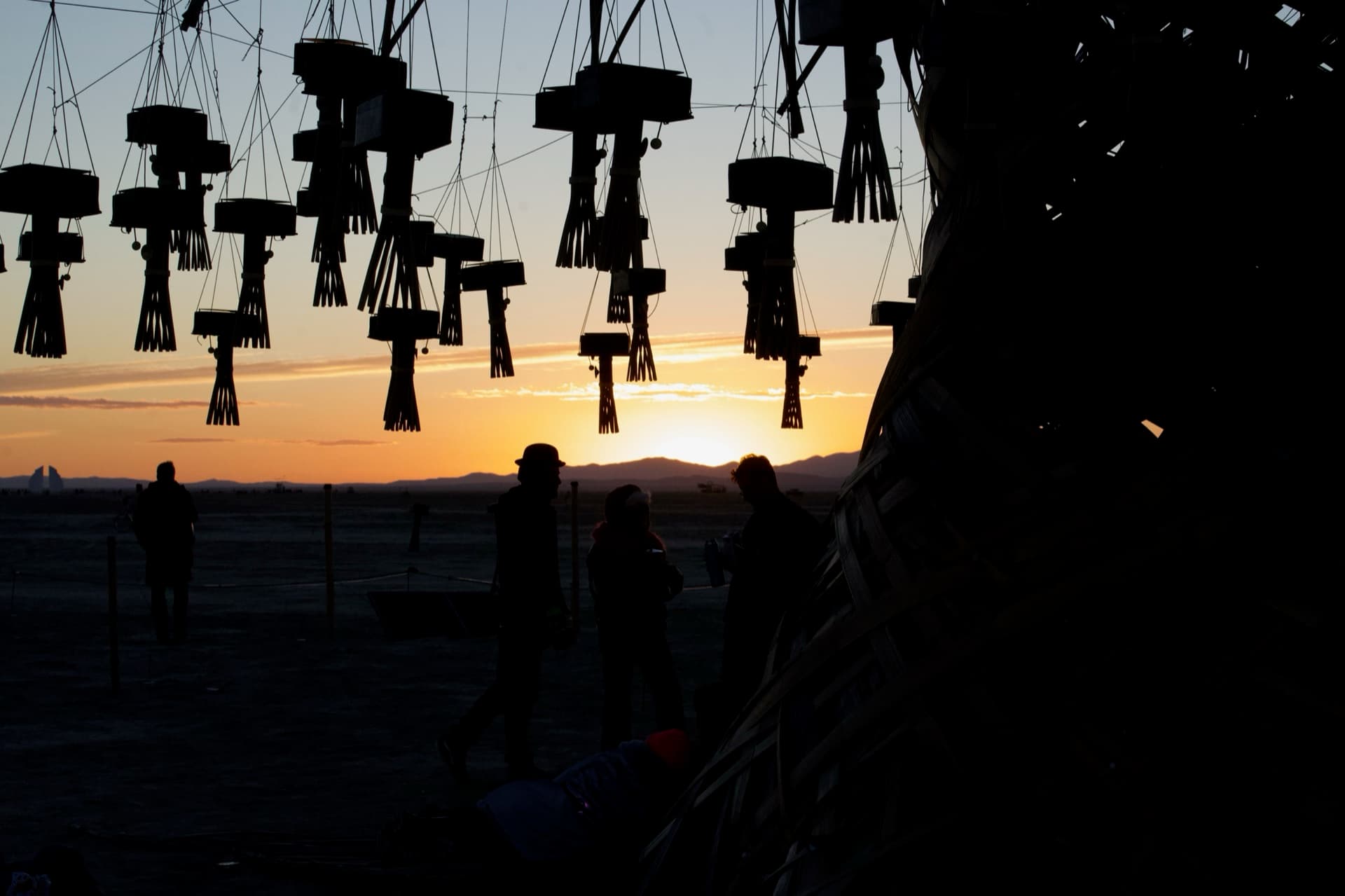 Sunset under the Resonance Tree at Burning Man 2026, silhouettes gathered beneath the lantern canopy
